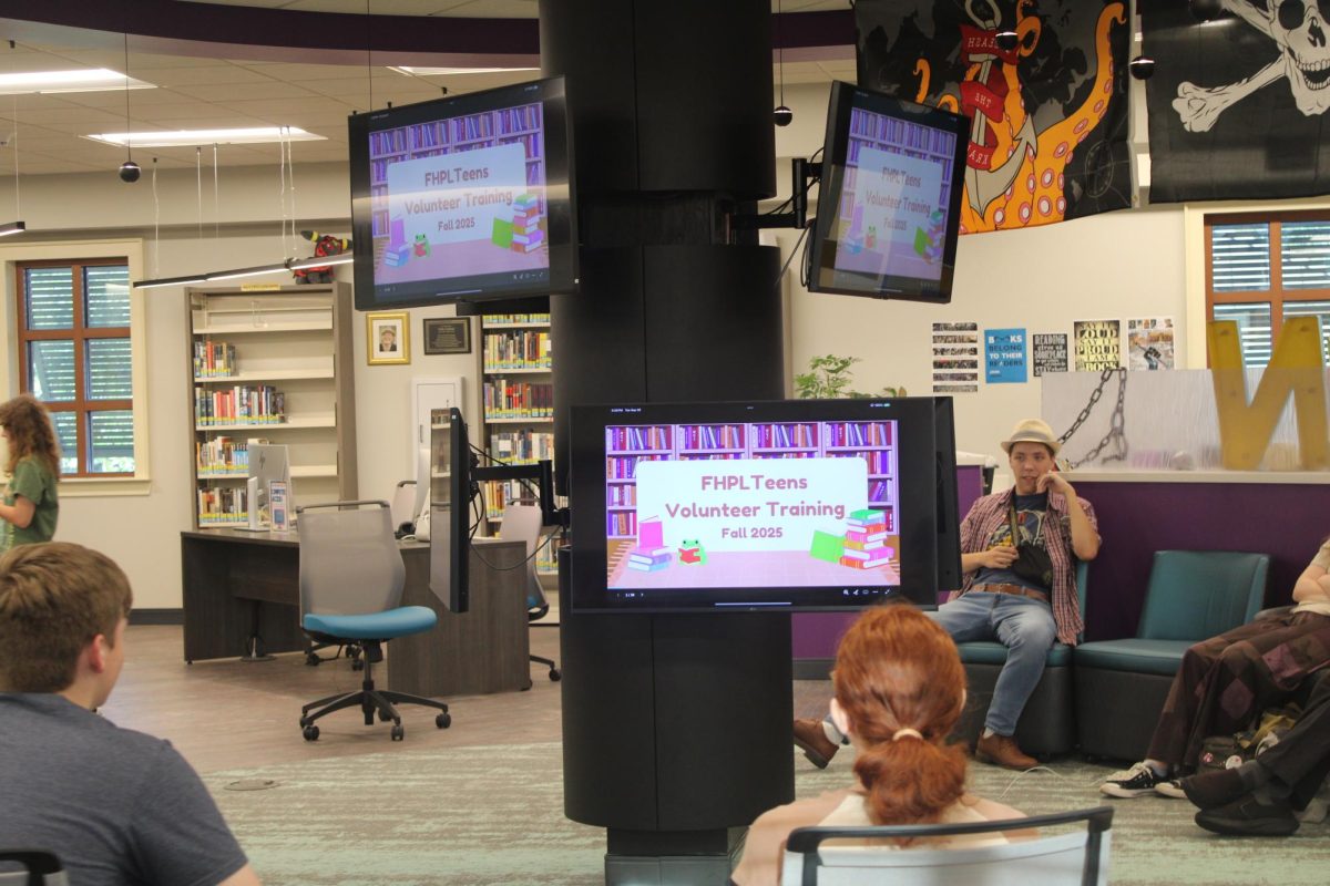 Gather Around… Teen volunteers lounge around the upstairs Teen Space at the Fairhope Public Library, where a slideshow presentation is on display in the background. The group helped train new members. (Sharon Smith)